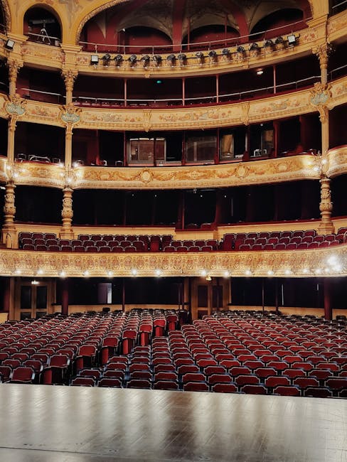 The interior of the Royal Opera House showing the main auditorium with multiple tiers of ornate, gold-accented balconies and private boxes. The stage area at the front features a hardwood floor with a